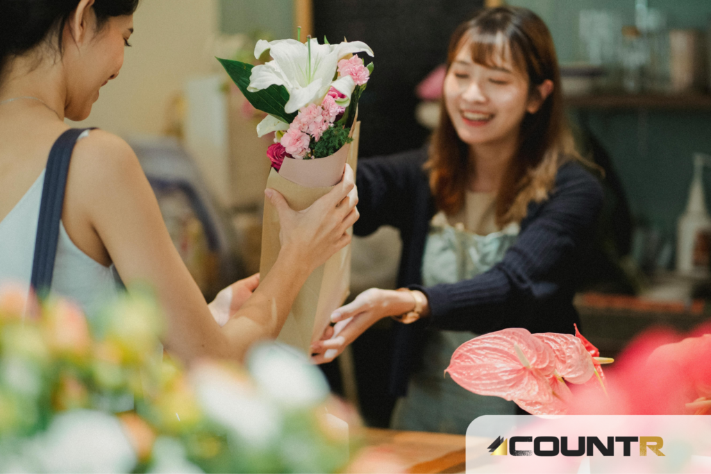 Smiling florist hands a bouquet to a returning customer at the counter