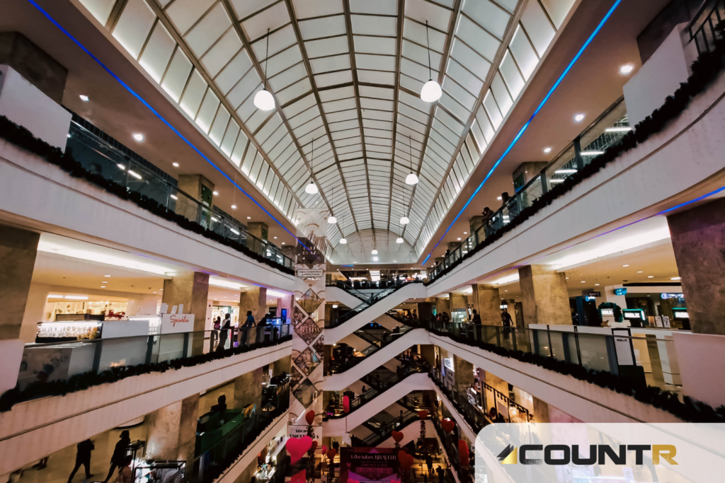 Interior view of a multi-level shopping mall with escalators and retail stores, illustrating a potential use case for CountR footfall analytics 