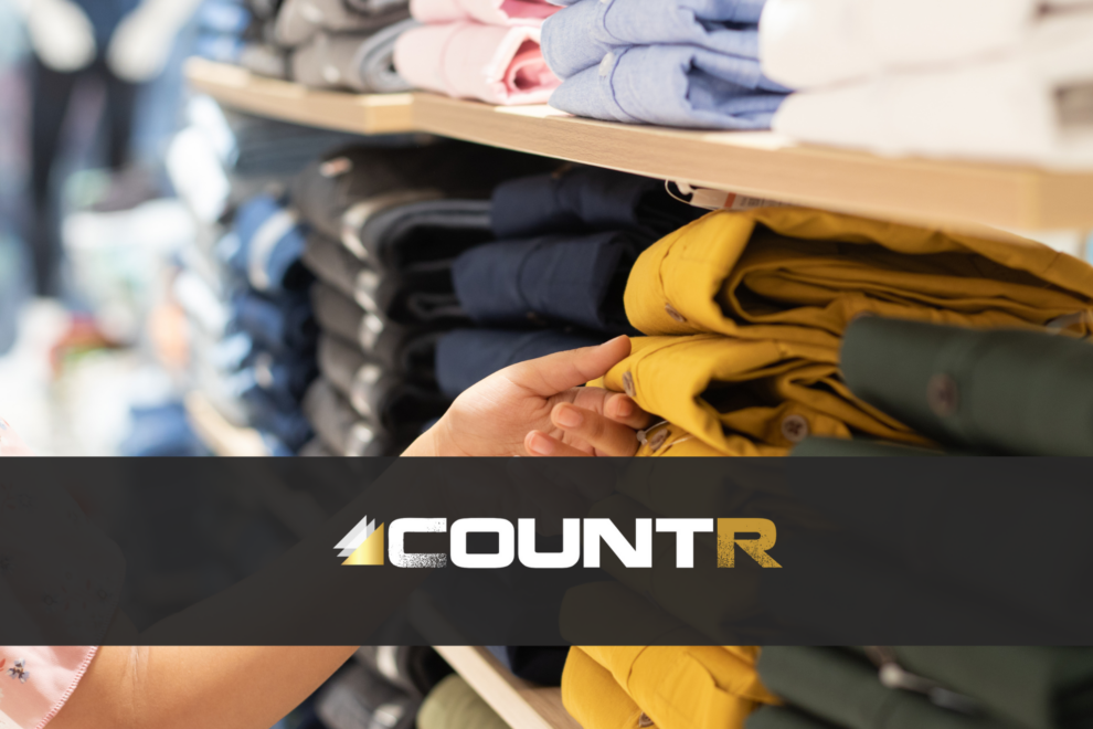 Customer hand selecting folded pants from a retail shelf in a clothing store