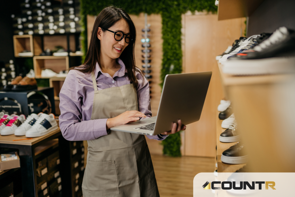 Female retail employee checking CountR analytics on a laptop inside a shoe store.
