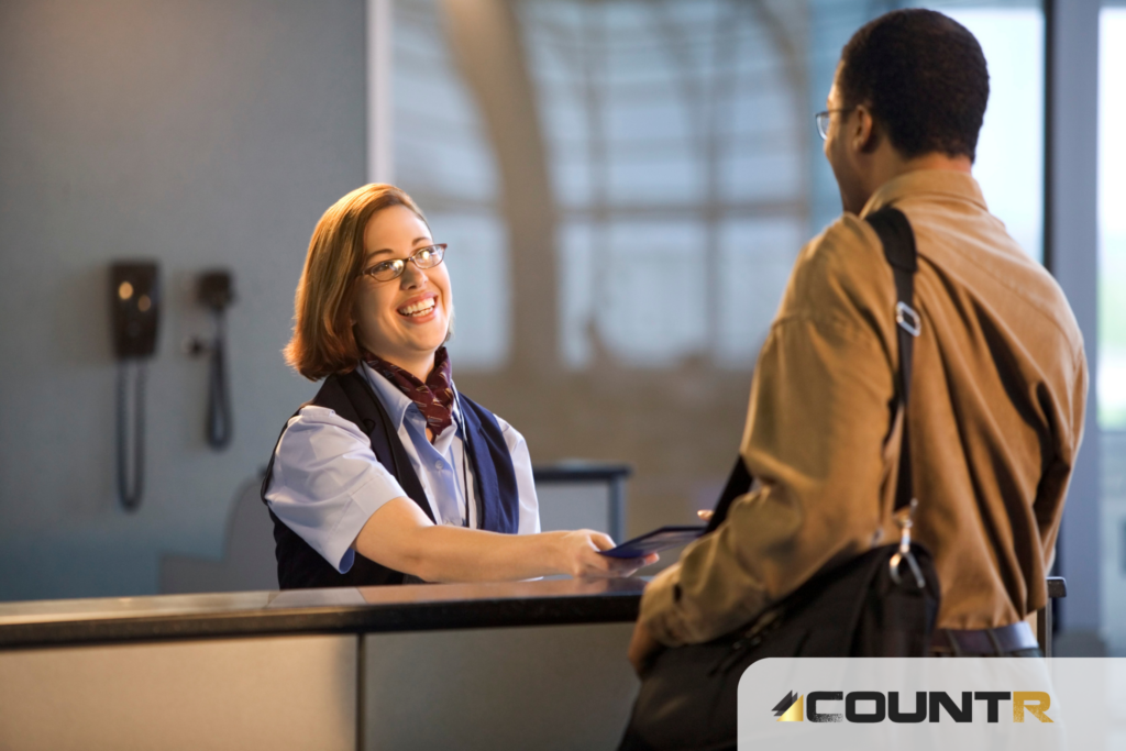 Smiling airport staff assisting a traveler at the check-in counter with CountR logo