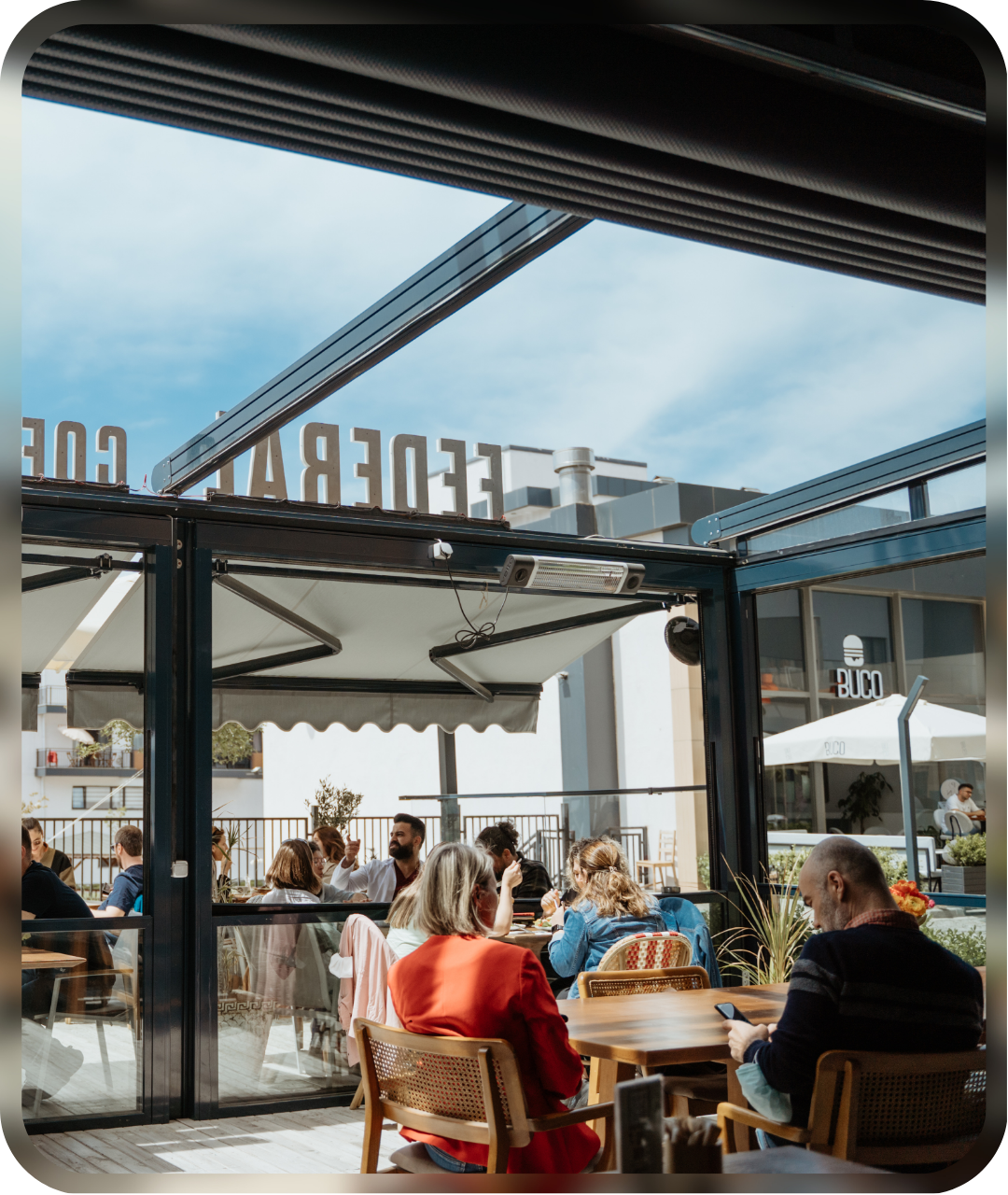People sitting at tables on a bright café terrace with open glass walls and natural light